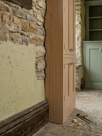 Fitted furniture being scribed to an irregular stone wall — rough shaping stage, old Cotswold property