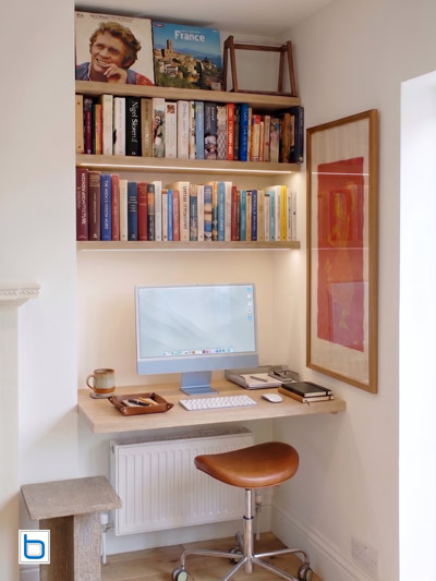 Compact custom home office installation inside a wall alcove featuring a floating wood desk, an iMac, and fitted bookshelves with LED underlighting.