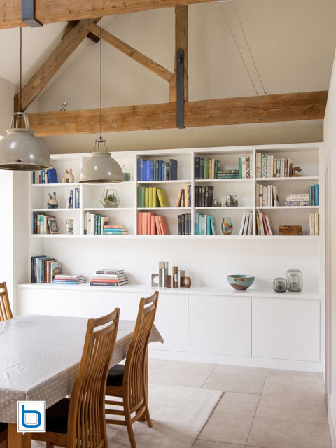 Fitted dining room furniture in large barn conversion — white shelving and base cabinets below exposed oak beams