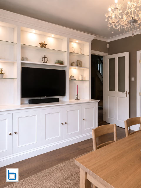 Fitted dining room furniture with open glass shelves, lighting, and central TV area — white period style