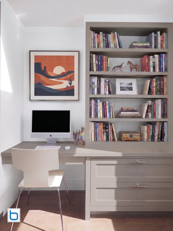 A small home office fitted in Farrow & Ball Elephant's Breath, with a floating desk, shaker drawers, and open shelving displaying books and framed prints.