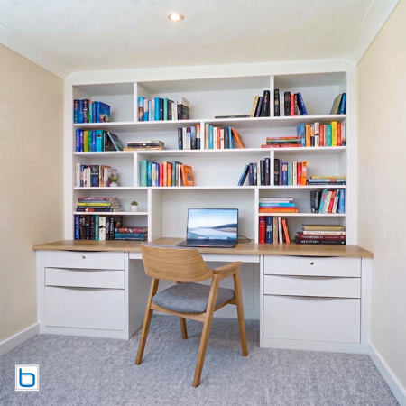 Contemporary White built-in cupboards with profile handles, a natural wood countertop, and integrated study shelving surrounding a laptop desk.