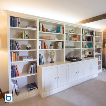 Large wall to wall fitted living room bookcase unit cream painted shaker cupboard doors and open shelving exposed beam ceiling
