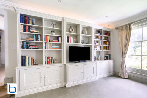Traditional white floor-to-ceiling entertainment wall with raised-panel cupboard doors, a central TV alcove, and elegant period pilasters.