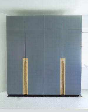 Bespoke contemporary wardrobes painted in Farrow & Ball Hague Blue, featuring full-height flat panel doors, integrated long oak timber handles, and a floor-to-ceiling configuration.