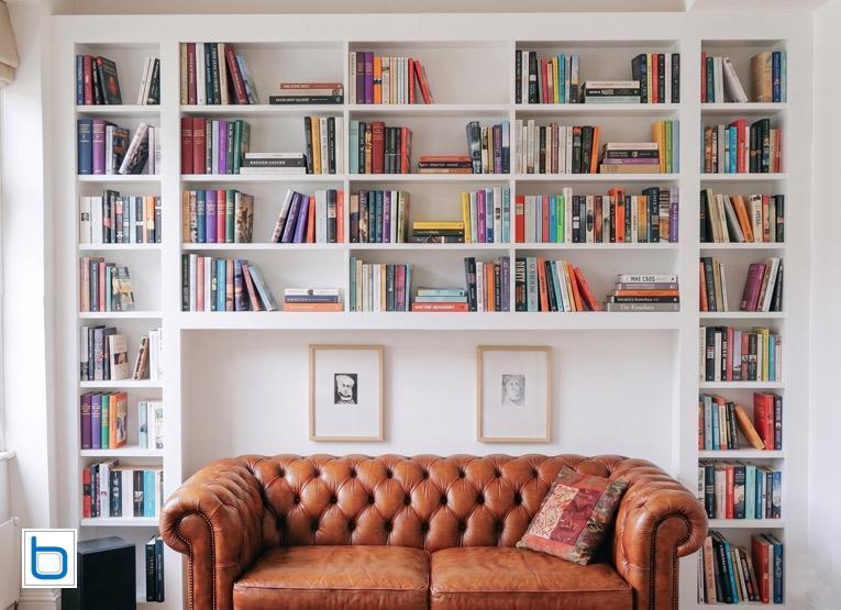 Bespoke built-in bookcases wall to wall in white — floor to ceiling open shelving with central breakfront section and Chesterfield sofa in a living room