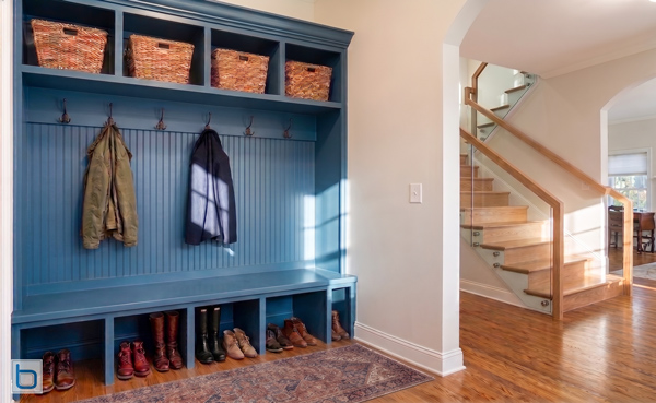 Bespoke blue hallway boot room storage unit featuring an integrated bench seat, lower shoe cubbies, coat hooks against a beadboard back, and top wicker basket shelves.