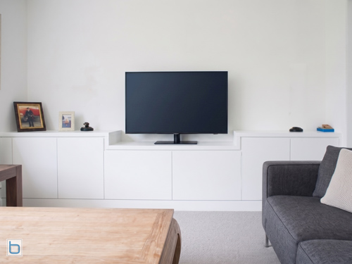 Bespoke white built-in cabinets configured as a modern, stepped low-level television console with handleless storage cupboards in a living room layout.