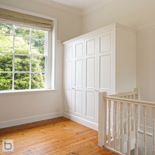 Bespoke white Victorian wardrobe featuring traditional multi-panelled doors, installed neatly on a spacious timber-floored hallway landing beside a staircase balustrade.