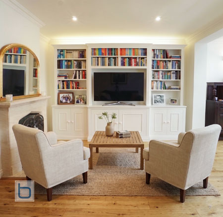 Custom white floor-to-ceiling media wall unit featuring a prominent breakfront central TV console section with matching shaker bookcases.