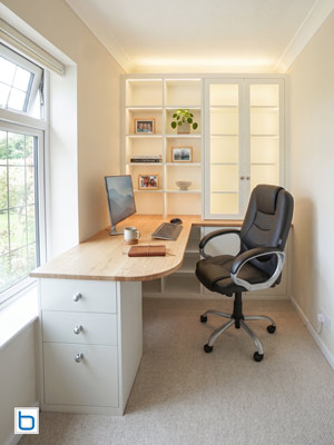 Compact home office installation featuring White built-in cupboards, an L-shaped Oak worktop desk, a glazed display cabinet, and LED uplighting.