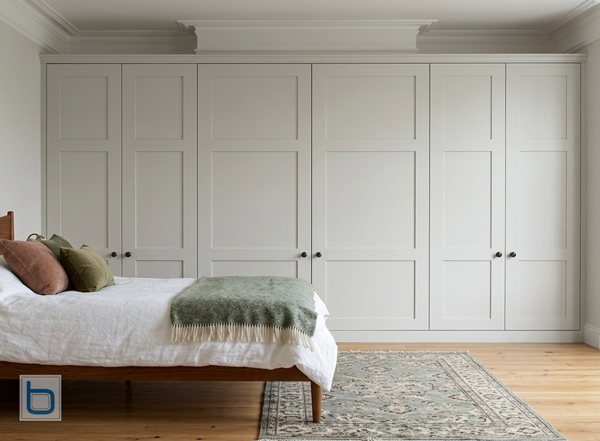Bespoke six-door Shaker wardrobes painted in Farrow & Ball Joa's White, featuring a shallower central section designed to fit seamlessly over a bedroom chimney breast.