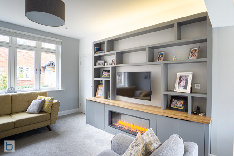 Custom Grey floor-to-ceiling entertainment center featuring an asymmetric bookcase, a natural wood countertop, a wall-mounted TV, and a linear electric fire.