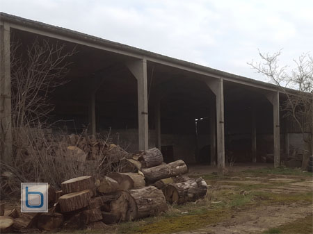 The original state of Built in Solutions workshop in Oxfordshire, featuring an old farm barn structure and timber logs before its transformation into a bespoke joinery workshop.