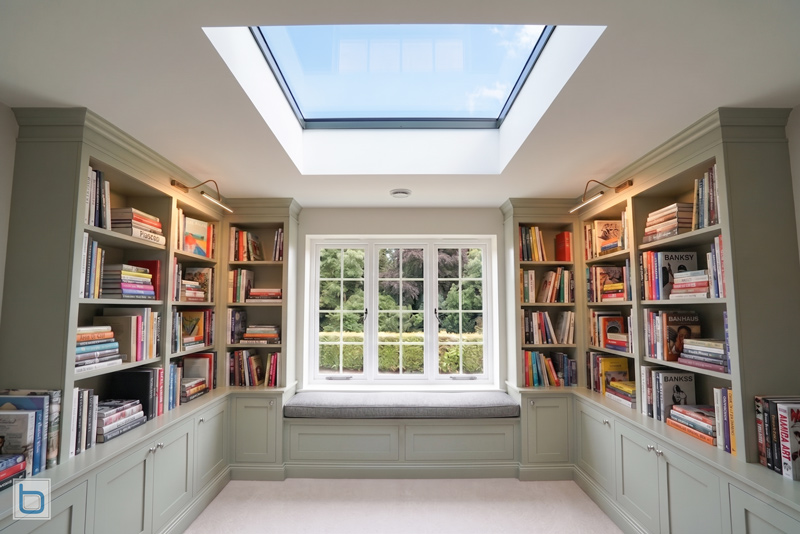 Fitted home library painted in Farrow and Ball Mizzle with floor-to-ceiling bookcases, integrated window seat, rooflight and inset panel base cupboards, Victorian extension