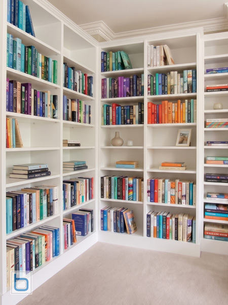 A custom white wrap-around corner bookcase featuring open floor-to-ceiling shelving filled with books, showing a seamless perpendicular junction and matching traditional crown moulding.