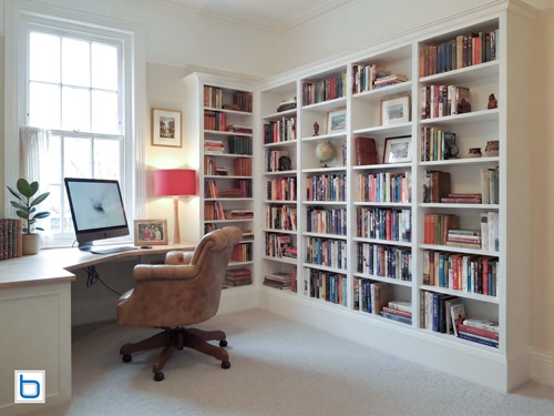 Custom white floor-to-ceiling corner bookcase wall integrated with a matching curved wooden top study desk in a home office.