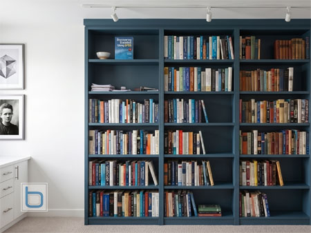 Custom multi-section fitted library bookcase painted in Farrow and Ball Hague Blue under track lighting.