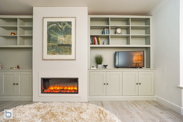 Bespoke Farrow and Ball green living room furniture showcasing a Strong White false chimney breast with an integrated electric fire, lower shaker cupboards, and matching bookshelves.