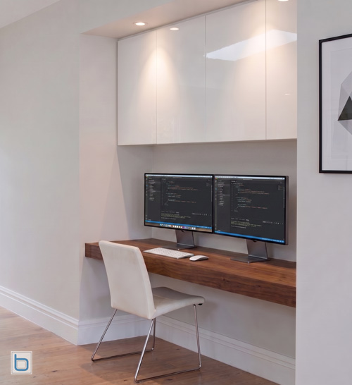 Bespoke modern home office workstation featuring high-gloss White built-in cupboards above a floating wood desk with a dual monitor setup.