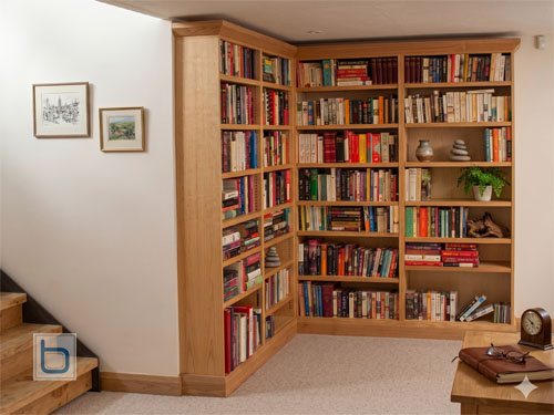Custom natural oak wrap-around corner library bookcase fitted seamlessly into a home interior next to a wooden staircase.