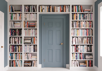 Custom white built-in library shelving unit framed symmetrically around a slate blue interior door.