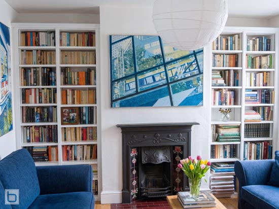 White built in bookcases filled with books either side of a black cast iron fireplace, with blue sofas and a coffee table in the living room.