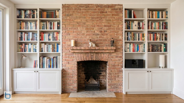 A sample photo showcasing custom built-in alcove shelving units with lower Shaker style storage cupboards flanking a traditional cast iron arched fireplace with a white mantel piece.