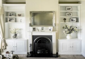 White painted fitted alcove cupboards either side of a period cast iron fireplace with open shelving and display objects above