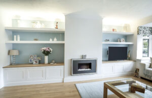 Custom low-profile white media cupboards flanking a central fireplace breast with floating light blue backed shelving.
