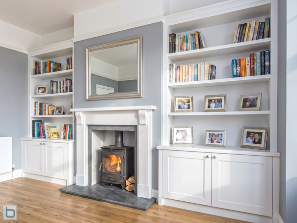 Custom-built white alcove units featuring traditional shaker base cupboards and open upper display shelving, flanking a classic white mantelpiece with an integrated log burner stove.