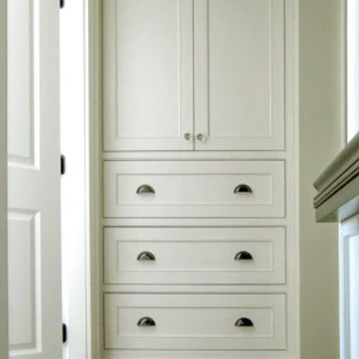 A bespoke fitted cupboard in a hallway alcove, painted pale sage green with shaker doors, cup pull handles, and a matching chest of drawers