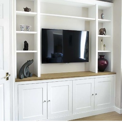 A bespoke fitted media unit with open alcove shelving either side of a wall mounted television, above white shaker style base cupboards and an oak worktop.