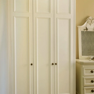 Close-up of cream painted fitted wardrobe doors with traditional brass knob handles, positioned beside a dressing table mirror.