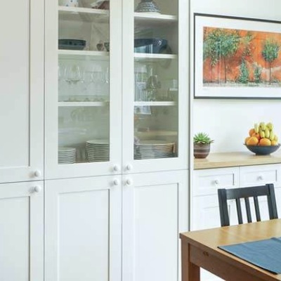 Close-up view of a white shaker style dresser with glass fronted cupboard doors displaying crockery, above closed base cupboards with a wooden worktop.