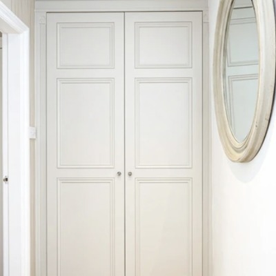Close-up of pale grey fitted wardrobe doors with a panelled design, positioned beside a round wall mounted mirror.