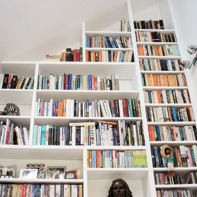 White fitted bookcases built into a sloped ceiling, with angled shelving following the roofline.