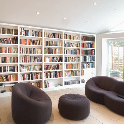 Fitted bookcases lining a bright garden room, furnished with curved sofas and looking out onto the garden.