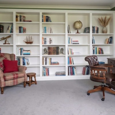 Fitted bookcases painted in sage green, with a leather armchair and writing desk in a home library.