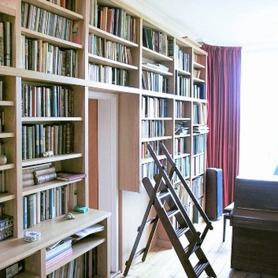 Fitted bookcases with a built in library ladder for reaching upper shelves, lining a hallway with a piano.