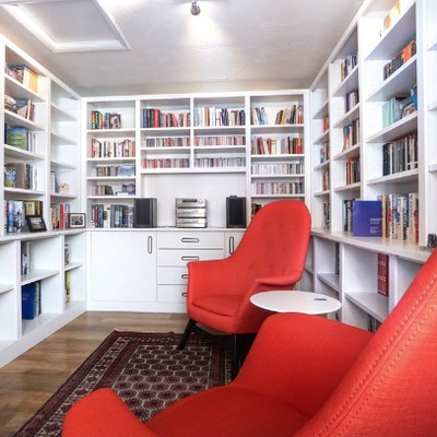 A fitted home library with a built in desk and shelving, furnished with two red armchairs and a rug.