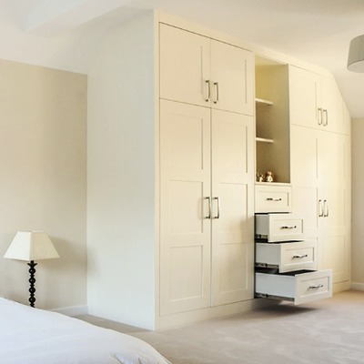 Fitted wardrobes with open shelving and pull-out drawers, built into a sloped ceiling bedroom with cream shaker doors.