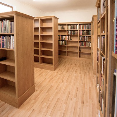 Oak library shelving Bookcase units arranged in rows along a long narrow room with wooden flooring.