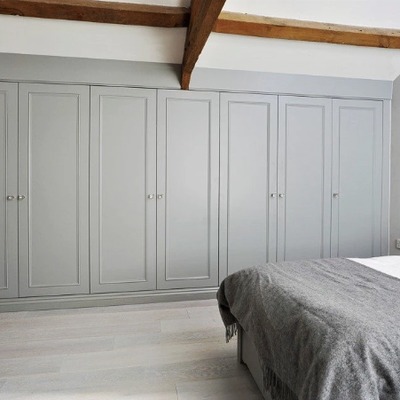 Grey fitted wardrobes built into a sloped ceiling bedroom with exposed wooden beams overhead.