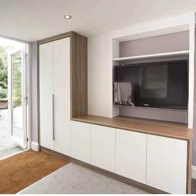 A modern fitted storage wall and media unit in a hallway, combining pale wood tall cupboards with white base units and an integrated oak worktop.