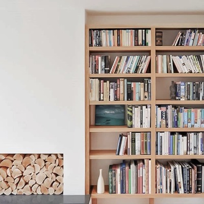 Natural oak fitted bookcases either side of a fireplace, with an integrated log store built into the base.