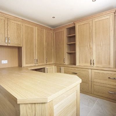 Oak fitted corner cabinets with panelled doors and drawers, alongside a central island unit with a worktop, shown mid installation with exposed sockets.