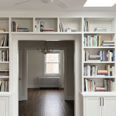 White fitted bookcases framing a doorway, with open shelving either side and a radiator built in below.
