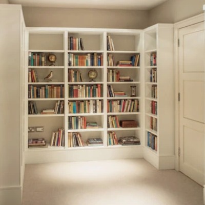 White fitted bookcases wrapping around a corner junction, with open shelving holding books and small ornaments.