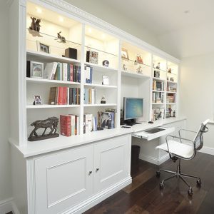 White painted fitted home office with integrated desk, floor-to-ceiling display shelving and closed base cupboards, Buckinghamshire